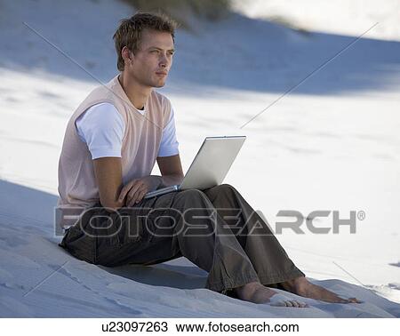 A young man on a beach working on a laptop View Large Photo Image Stock Image - A young man on a beach working on a laptop. Fotosearch