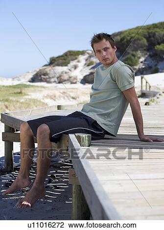 A young man sitting on a beach View Large Photo Image Stock Image - A young man sitting on a beach. Fotosearch