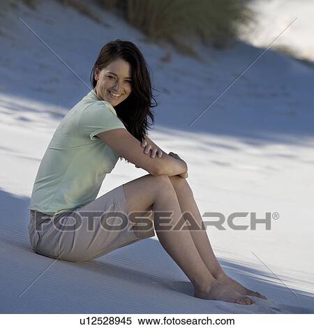 Stock Photography - A young woman sitting alone on a beach. Fotosearch