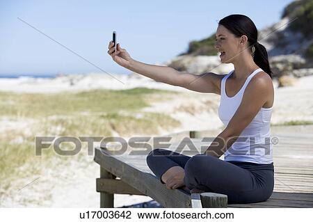 A young woman taking a photo of herself with a mobile phone View Large Photo Image Stock Image - A young woman taking a photo of herself with a mobile phone. Fotosearch