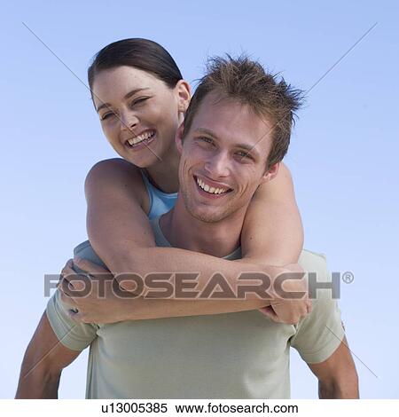 Stock Photography - Portrait of a young couple, man giving woman piggyback. Fotosearch