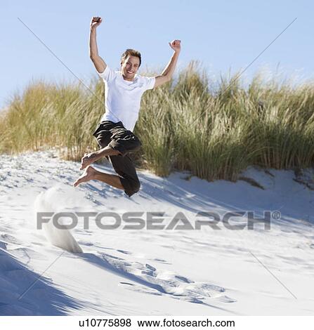 Stock Photo - Young man jumping in sand dunes. Fotosearch