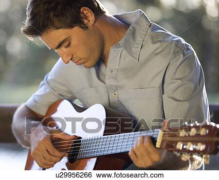 A young man playing a guitar View Large Photo Image Stock Photograph - A young man playing a guitar. Fotosearch