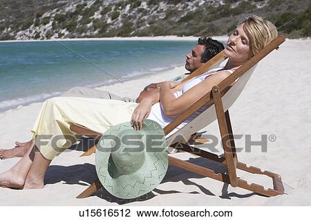 Stock Image - A mature couple relaxing in deckchairs on a beach. Fotosearch