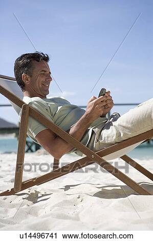 Stock Image - A mature man sitting in a deck chair on a cell phone. Fotosearch