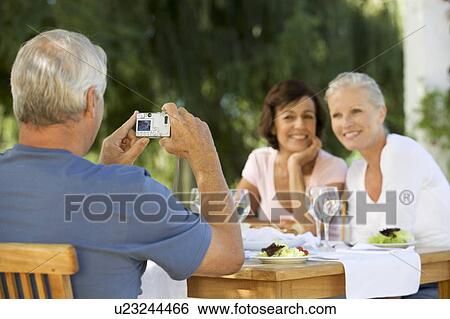 Stock Photograph - A group of senior couples at a restaurant, man taking picture with digital camera. Fotosearch