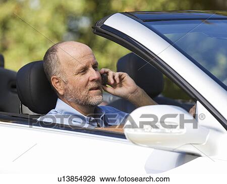 A senior man driving a car whilst on a cell phone View Large Photo Image Stock Photo - A senior man driving a car whilst on a cell phone. Fotosearch