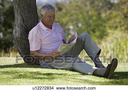 A senior man sitting under a tree reading a newspaper View Large Photo Image Picture - A senior man sitting under a tree reading a newspaper. Fotosearch