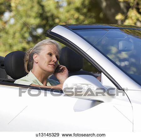 A senior woman driving a car whilst on a cell phone View Large Photo Image Stock Photo - A senior woman driving a car whilst on a cell phone. Fotosearch