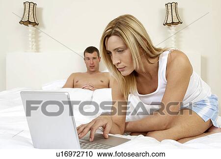 Stock Image - Young couple in bedroom, working on laptop. Fotosearch