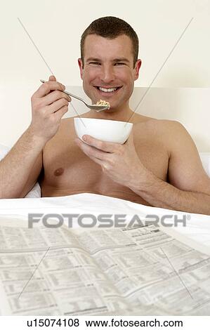 Young man in bed eating breakfast and reading the papers View Large Photo Image Stock Photo - Young man in bed eating breakfast and reading the papers. Fotosearch