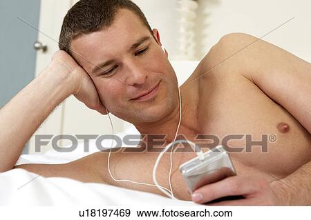 Stock Photo - Young man in bed listening to music. Fotosearch