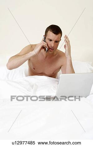 Stock Photography - Young man in bed, working on laptop. Fotosearch