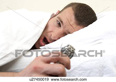 Young man laying in bed, looking at watch View Large Photo Image Stock Photo - Young man laying in bed, looking at watch. Fotosearch