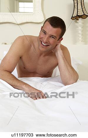 Stock Image - Young man sitting up in bed, laughing. Fotosearch