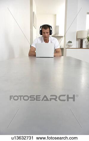 Stock Image - Young man working from home, listening to music. Fotosearch