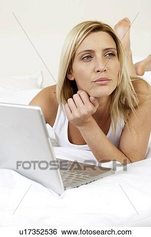 Stock Photograph - Young woman in bed working on laptop. Fotosearch