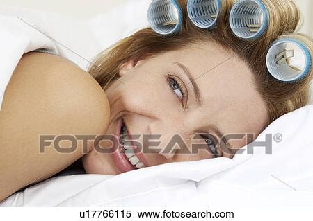 Stock Photography - Young woman laying in bed with curlers in hair. Fotosearch