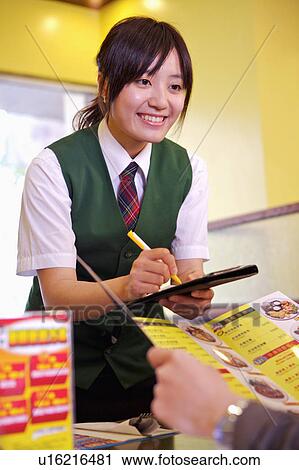 Stock Image - Young waitress serving for the customer and smiling, Restaurant. Fotosearch