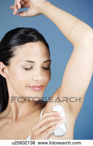 Stock Photo - A young woman applying a de-odorant . Fotosearch