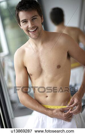 Young man measuring his waist View Large Photo Image Stock Photo - Young man measuring his waist. Fotosearch