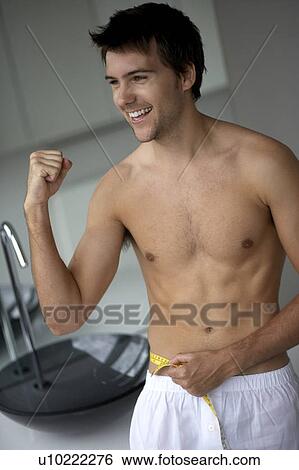 Young man measuring his waist View Large Photo Image Stock Photograph - Young man measuring his waist. Fotosearch