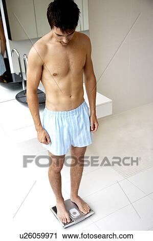 Stock Image - Young man standing on bathroom scales. Fotosearch