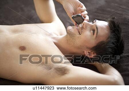Young man laying on a bed talking on a mobile phone View Large Photo Image Stock Image - Young man laying on a bed talking on a mobile phone. Fotosearch