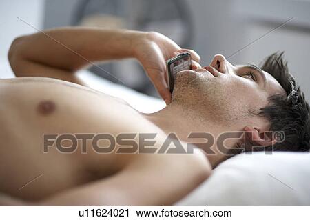 Young man laying on a bed talking on a mobile phone, close-up View Large Photo Image Stock Image - Young man laying on a bed talking on a mobile phone, close-up. Fotosearch