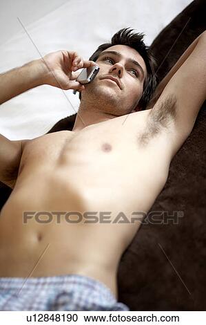 Stock Image - Young man laying on a bed talking on a mobile phone. Fotosearch
