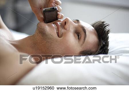 Young man laying on a bed talking on a mobile phone, close-up View Large Photo Image Stock Image - Young man laying on a bed talking on a mobile phone, close-up. Fotosearch