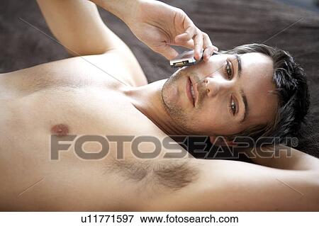 Young man laying on a bed talking on a mobile phone View Large Photo Image Stock Photo - Young man laying on a bed talking on a mobile phone. Fotosearch
