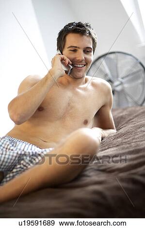 Young man laying on a bed talking on a mobile phone View Large Photo Image Stock Photo - Young man laying on a bed talking on a mobile phone. Fotosearch