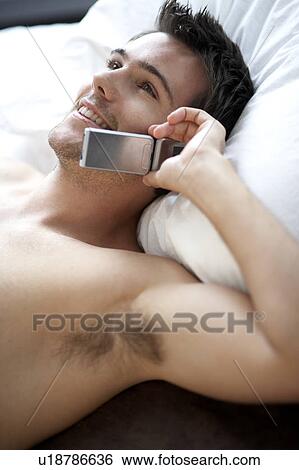 Stock Photograph - Young man laying on a bed talking on a mobile phone. Fotosearch