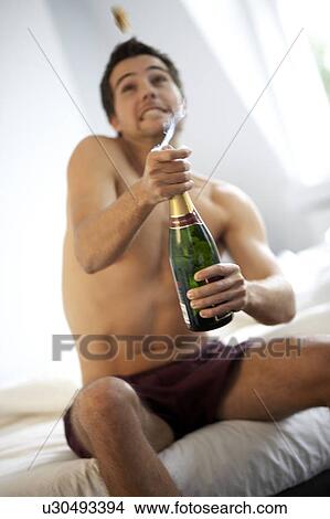 Young man opening a bottle of champagne in the bedroom View Large Photo Image Picture - Young man opening a bottle of champagne in the bedroom. Fotosearch