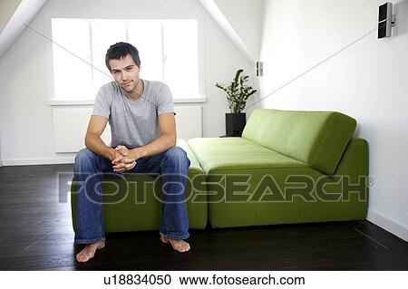 Stock Image - Young man sitting in a bedroom. Fotosearch