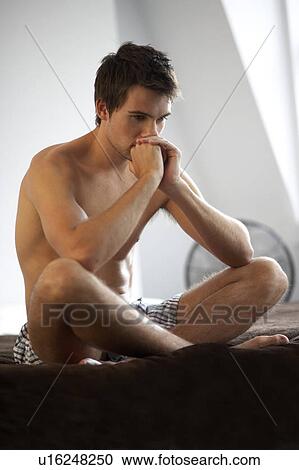 Young man sitting on a bed View Large Photo Image Stock Image - Young man sitting on a bed. Fotosearch