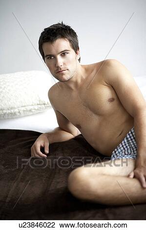 Young man sitting on a bed View Large Photo Image Stock Image - Young man sitting on a bed. Fotosearch