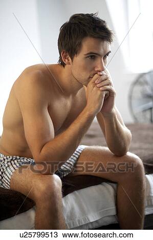 Young man sitting on a bed View Large Photo Image Stock Image - Young man sitting on a bed. Fotosearch