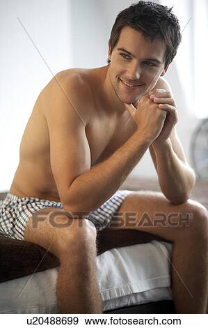 Young man sitting on a bed View Large Photo Image Stock Photo - Young man sitting on a bed. Fotosearch
