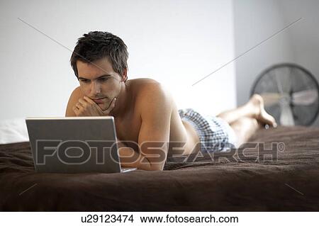 Young man with a laptop, laying on a bed View Large Photo Image Picture - Young man with a laptop, laying on a bed. Fotosearch