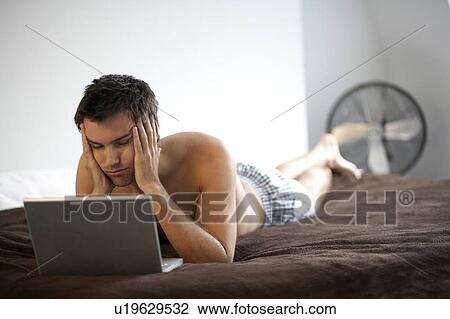 Stock Image - Young man with a laptop, laying on a bed. Fotosearch