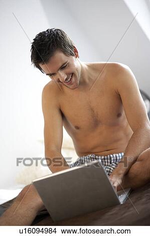 Young man with a laptop, sitting on a bed View Large Photo Image Picture - Young man with a laptop, sitting on a bed. Fotosearch