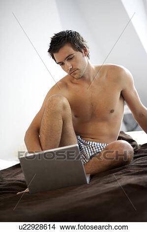 Young man with a laptop, sitting on a bed View Large Photo Image Picture - Young man with a laptop, sitting on a bed. Fotosearch