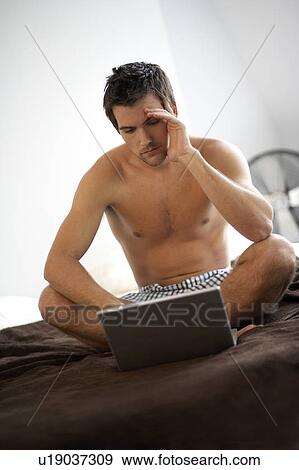 Young man with a laptop, sitting on a bed View Large Photo Image Stock Photo - Young man with a laptop, sitting on a bed. Fotosearch
