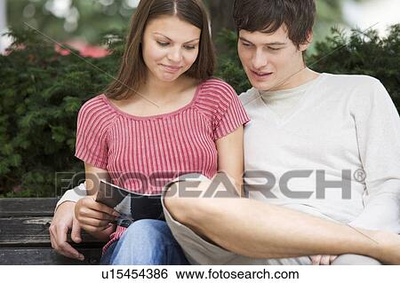 Stock Photograph - A young couple sitting on a park bench. Fotosearch