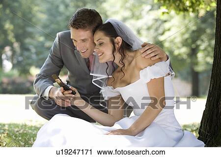 Stock Image - A bride and groom using a mobile phone. Fotosearch