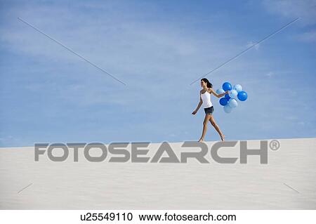 A woman walking in the desert holding a bunch of balloons View Large Photo Image Stock Image - A woman walking in the desert holding a bunch of balloons. Fotosearch