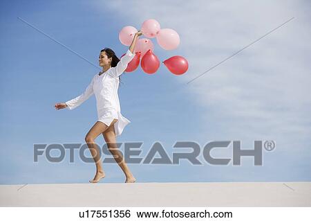 Stock Photograph - A woman walking in the desert holding a bunch of balloons. Fotosearch