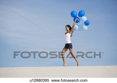 A woman walking in the desert holding a bunch of balloons View Large Photo Image Stock Photography - A woman walking in the desert holding a bunch of balloons. Fotosearch